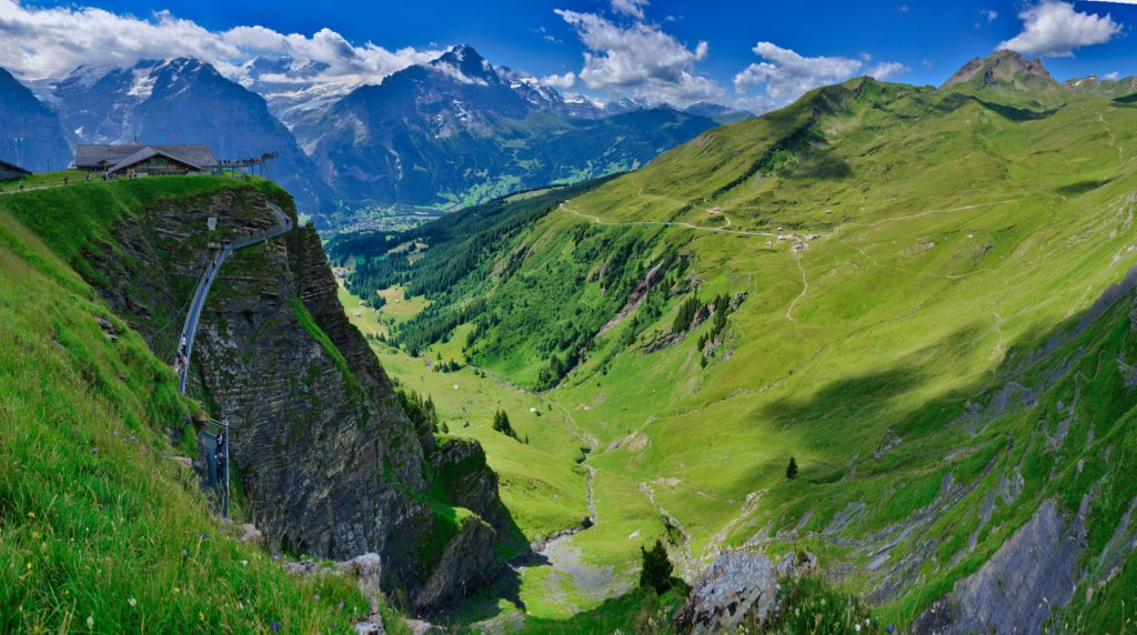 A stunning mountain valley on a clear, sunny day in First, Switzerland, where paragliding is often done for sport. This image is used in the Students Fare student travel blog, "Best Paragliding Destinations," which is a travel guide for paragliding all around the world.