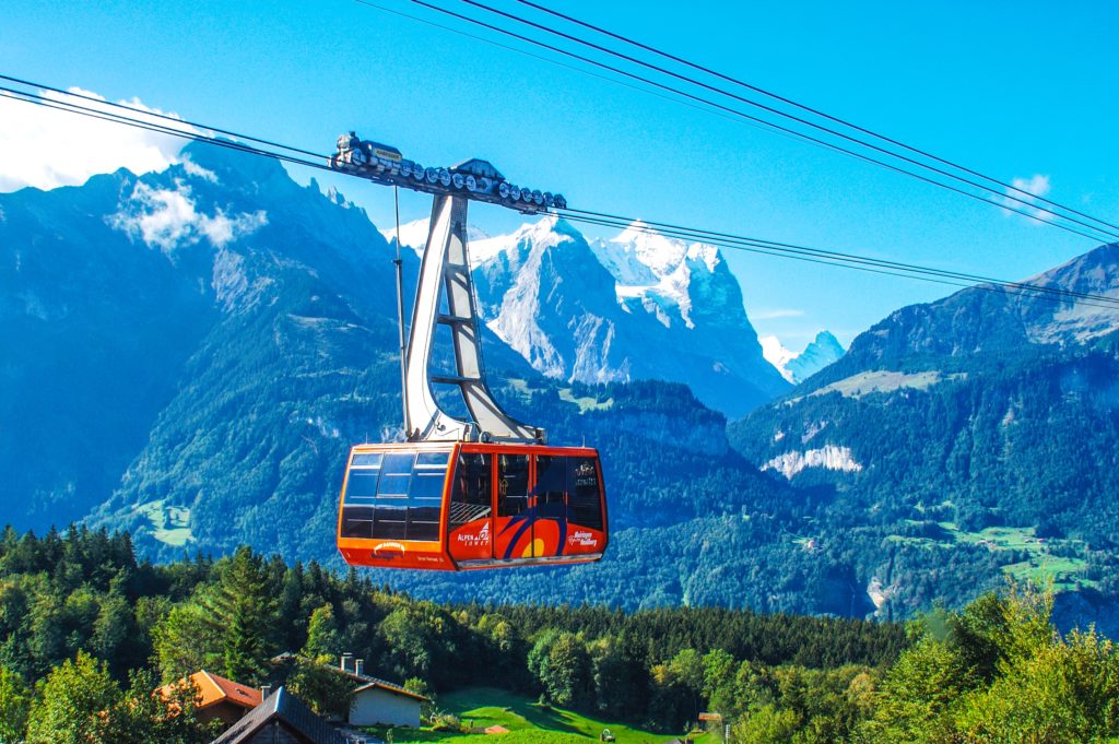 In the vibrant Swiss Alps, a cable car rides between two ski slopes and transports people on their college spring break. This image is used in the Students Fare student travel blog, "Spring Break in Switzerland," which is a travel guide to celebrating spring vacation in the Swiss Alps.