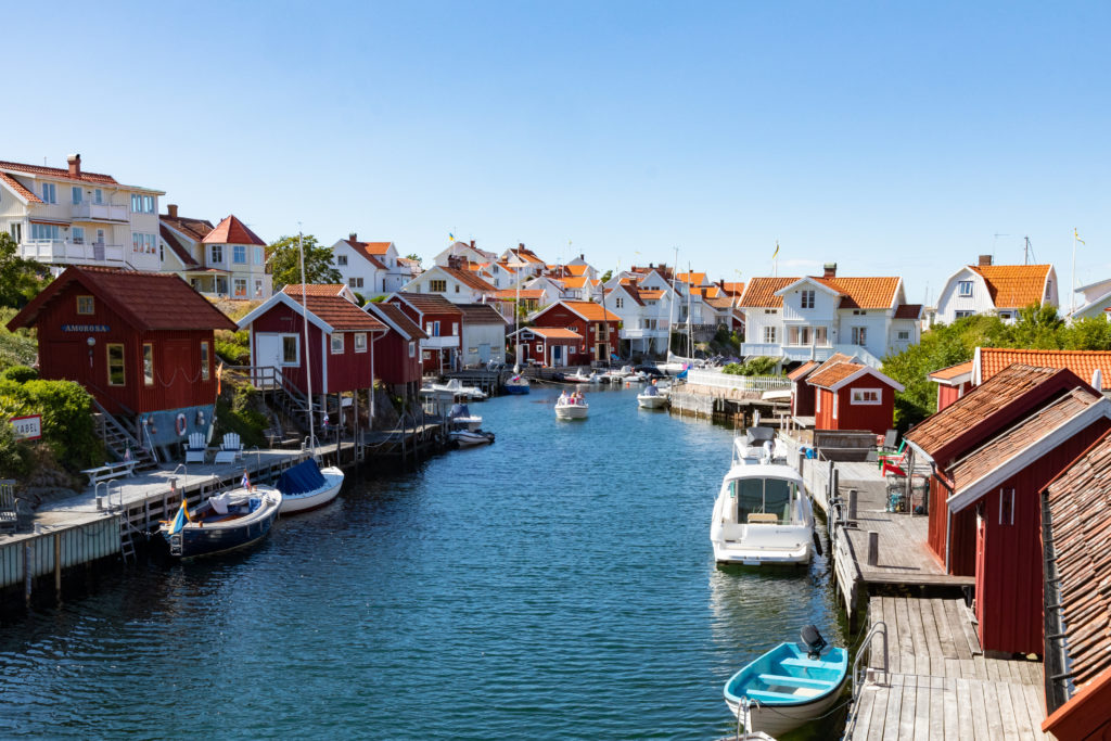 The beautiful landscape of Grundsund Bohuslän, in West Coast Sweden, with a river running between residential houses with white shingles and red roofs. This image is used in the Students Fare student travel blog, "Midsummer in Sweden," which describes the traditional festival and how to celebrate it.