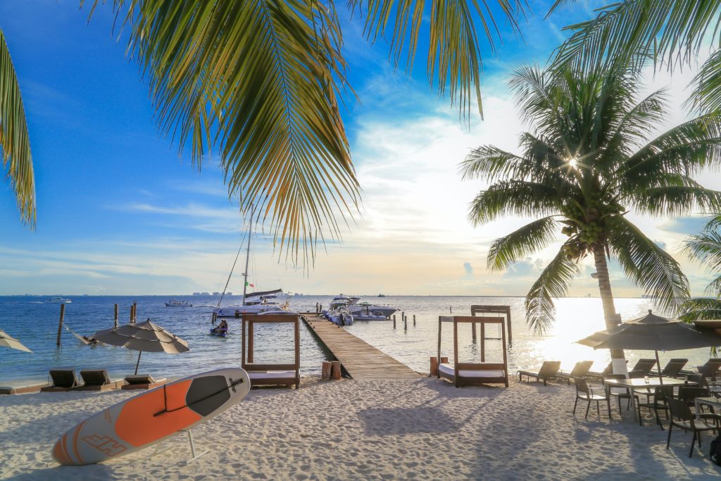 A landscape of the beach in Cancun, Mexico with white sand, clear water, sunny skies, and boats near a small dock. This image is featured in the travel blog by Students Fare, "Best Destinations for Group Vacations," which lists the top locations for youth and student groups to travel!