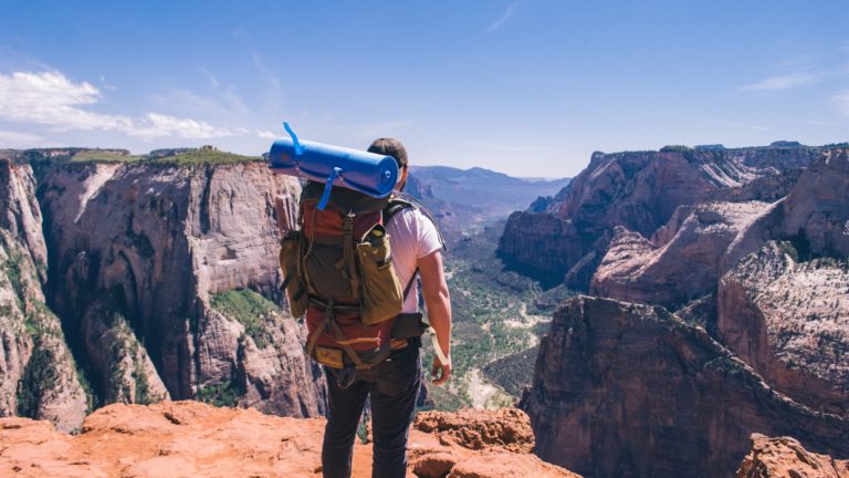 Featured in the Backpacking Guide for Students by Students Fare, this image shows a young man hiking a mountain on a backpacking trip.