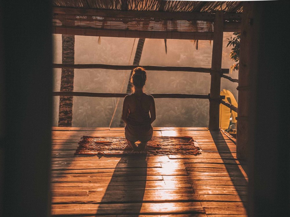 A female student traveler silhouetted against the warm sun practicing yoga.