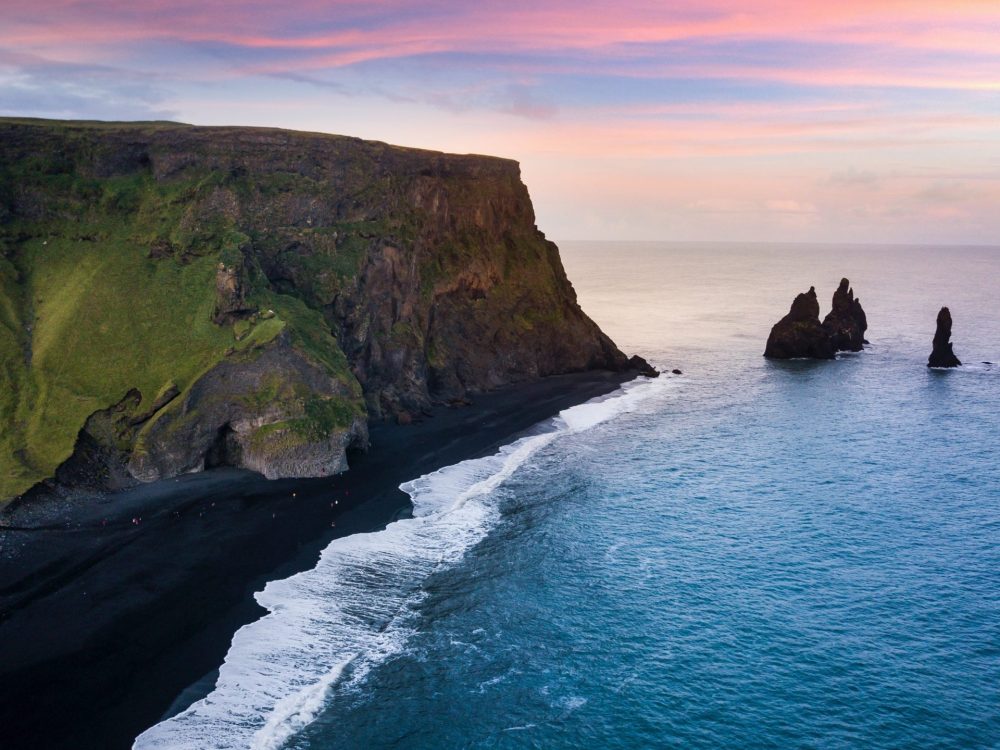 A tour view of the cliffside of student travelers walking along Reynisfjara Black Sand Beach in Vik, Iceland.