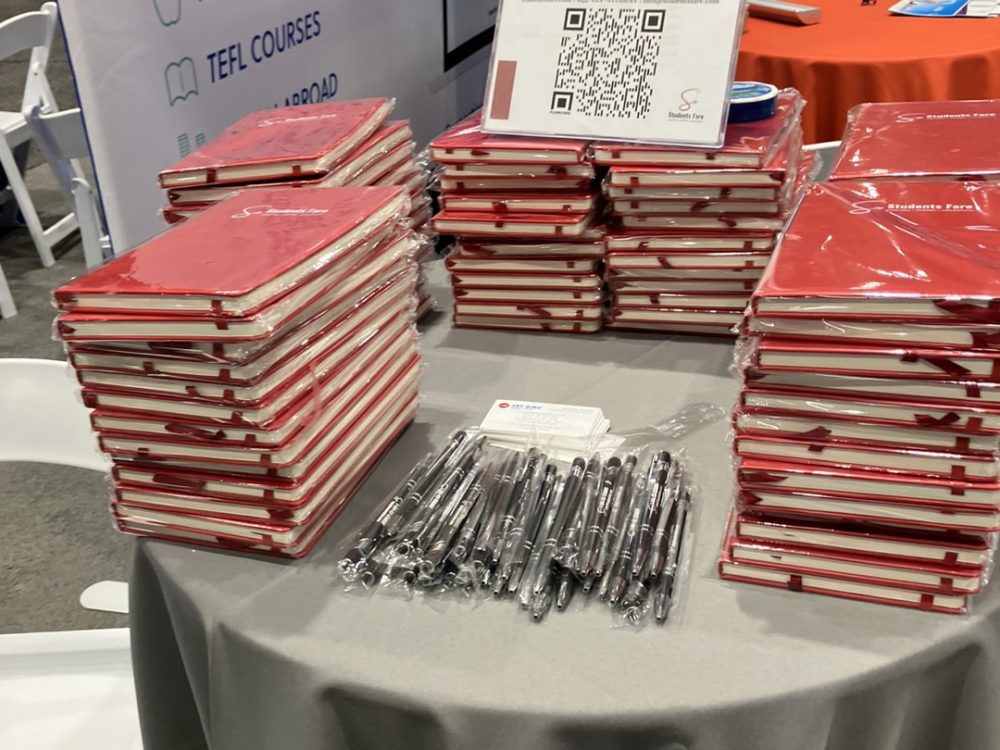 Notebooks and pen takeaways at the table where the Students Fare team members attended the NAFSA 2024 Annual Conference & Expo to discuss tours, flights, hotels, and academic pursuits.
