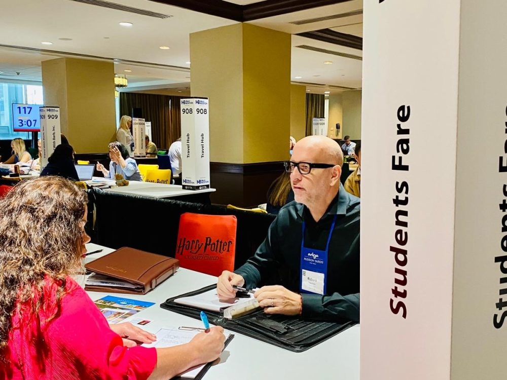 Two people sitting at the 2024 SYTA event for Students Fare to discuss flights, tours, hotels, and academic pursuits.